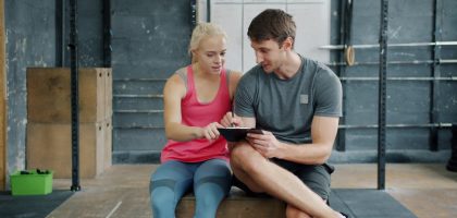 Man professional instructor is talking to young woman and writing in chart relaxing after training, people are waring trendy sports clothing and footwear.
