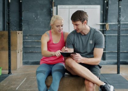 Man professional instructor is talking to young woman and writing in chart relaxing after training, people are waring trendy sports clothing and footwear.